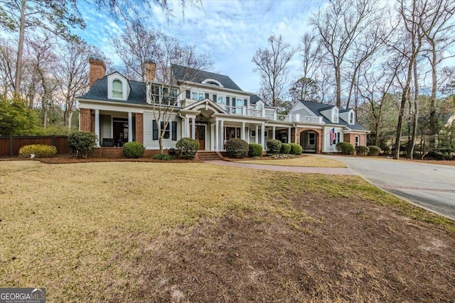 view of front of property featuring brick siding, a chimney, a front yard, fence, and a balcony