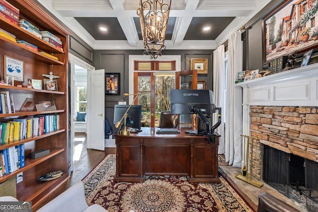 office area featuring beam ceiling, ornamental molding, a stone fireplace, wood finished floors, and coffered ceiling