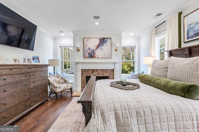 bedroom featuring dark wood-style floors, crown molding, a fireplace, and visible vents