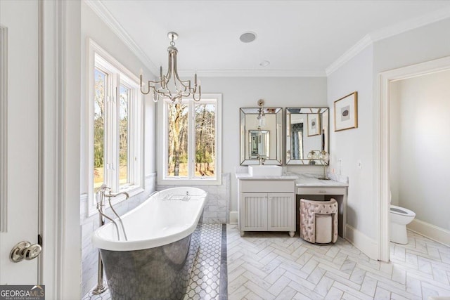 bathroom featuring a notable chandelier, a freestanding bath, toilet, ornamental molding, and vanity