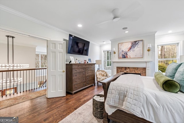 bedroom with dark wood-style floors, recessed lighting, crown molding, and a stone fireplace