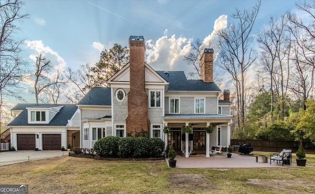 rear view of house featuring a garage, fence, concrete driveway, a lawn, and a chimney