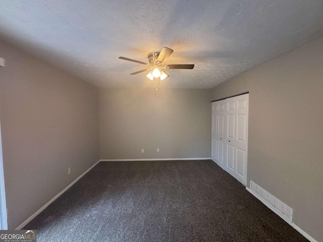 unfurnished bedroom with a textured ceiling, dark colored carpet, visible vents, and baseboards