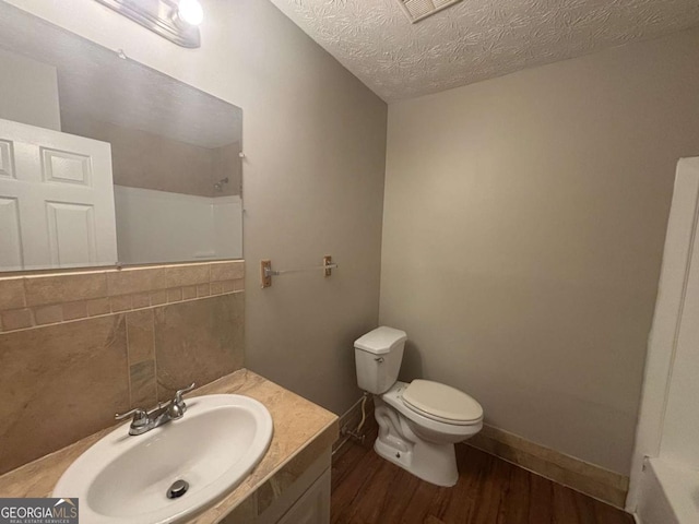 bathroom featuring a shower, toilet, wood finished floors, a textured ceiling, and vanity