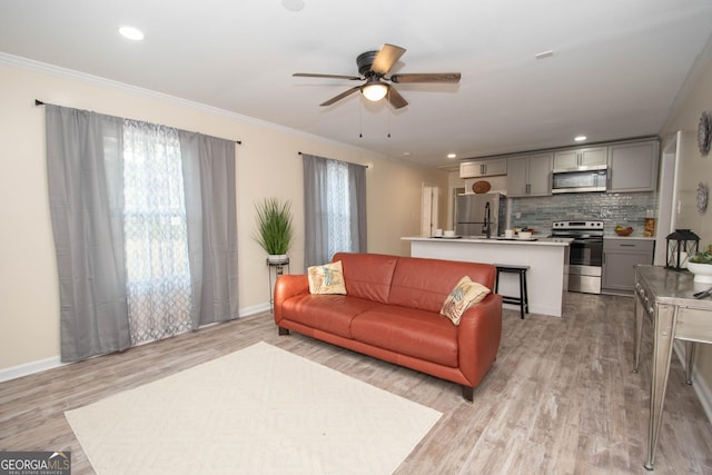 living room featuring baseboards, light wood-style floors, ornamental molding, and a ceiling fan