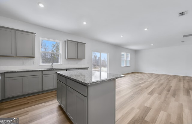 kitchen with backsplash, gray cabinetry, a kitchen island, a sink, and light wood-type flooring