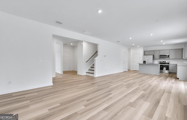 unfurnished living room featuring recessed lighting, visible vents, baseboards, stairway, and light wood-type flooring