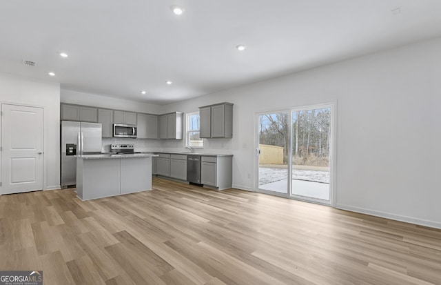 kitchen with a center island, stainless steel appliances, gray cabinets, visible vents, and light wood-style floors