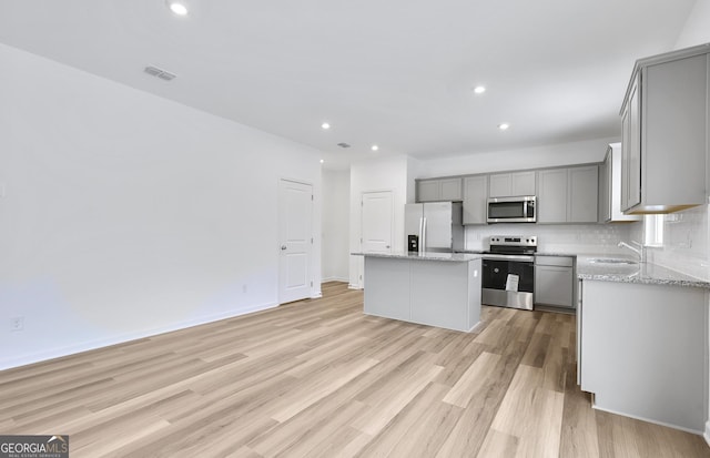 kitchen with appliances with stainless steel finishes, gray cabinets, a kitchen island, and backsplash