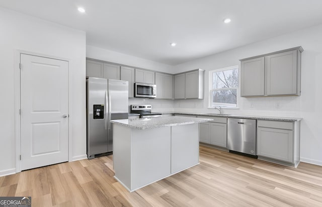 kitchen featuring light wood-style flooring, stainless steel appliances, a sink, gray cabinets, and tasteful backsplash