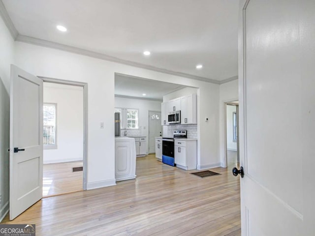 kitchen with light wood-style floors, white cabinets, appliances with stainless steel finishes, backsplash, and crown molding