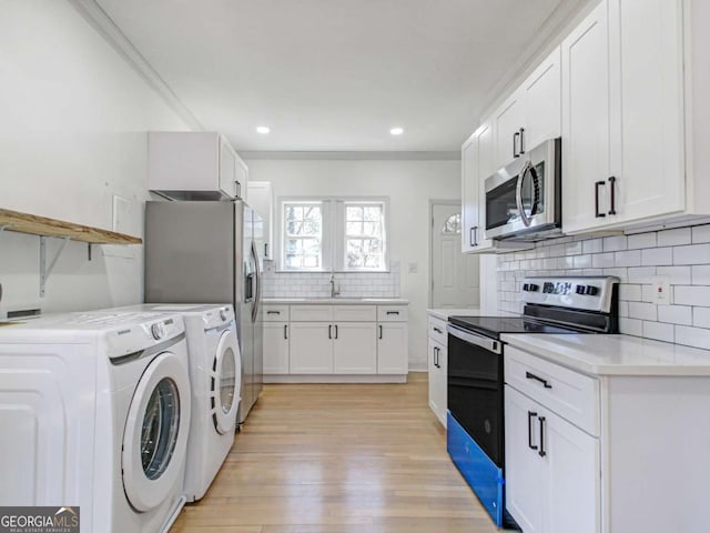 interior space featuring laundry area, light wood finished floors, ornamental molding, separate washer and dryer, and a sink