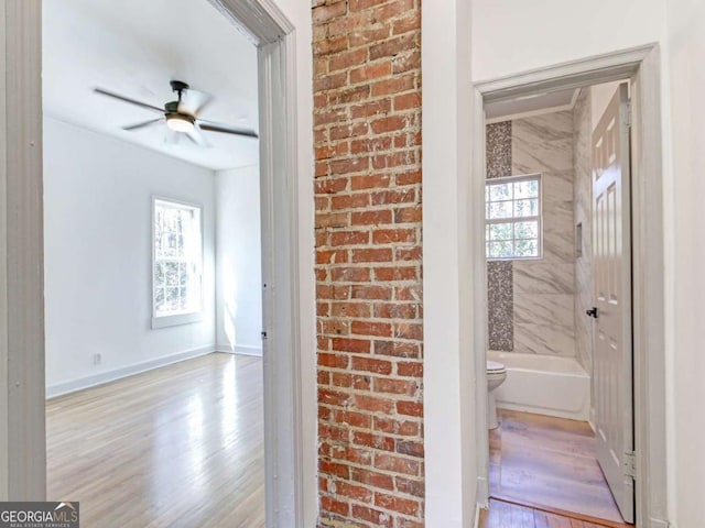 bathroom with toilet, brick wall, wood finished floors, a ceiling fan, and baseboards