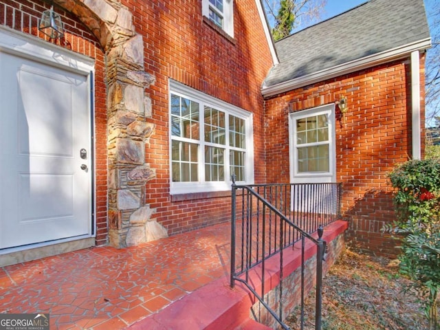 doorway to property with a shingled roof and brick siding