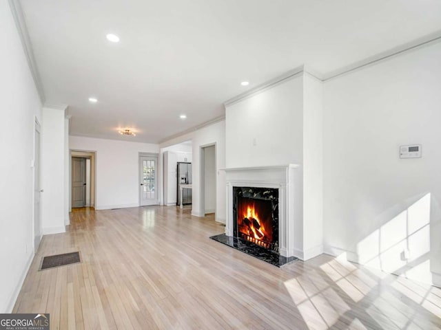 unfurnished living room featuring visible vents, baseboards, a premium fireplace, ornamental molding, and light wood-style floors