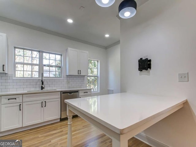 kitchen with tasteful backsplash, light countertops, crown molding, stainless steel dishwasher, and a sink