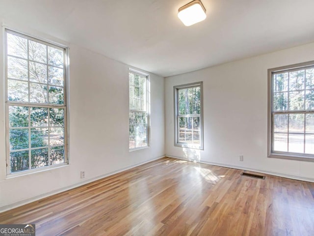 empty room featuring wood finished floors, visible vents, and a healthy amount of sunlight