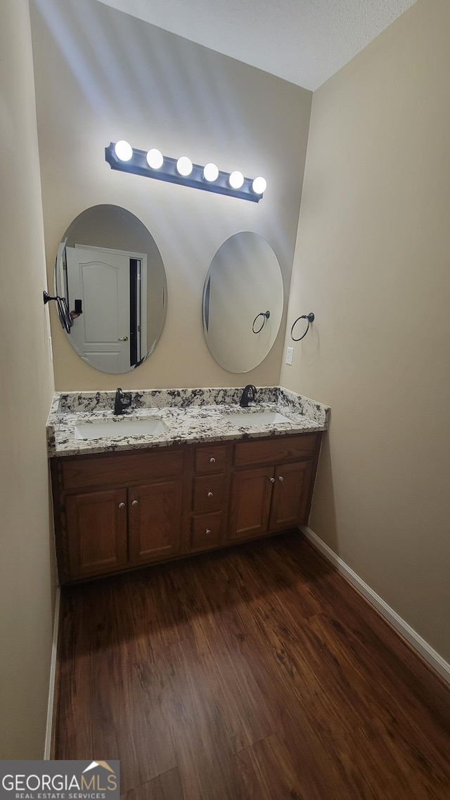 bathroom with double vanity, a sink, baseboards, and wood finished floors