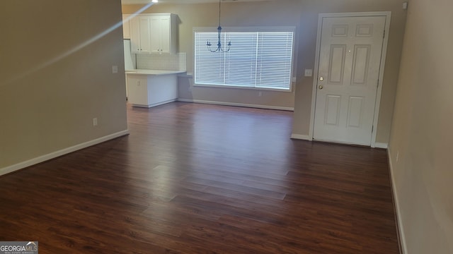 unfurnished living room with baseboards, dark wood-style flooring, and a notable chandelier