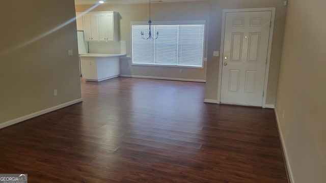 unfurnished dining area featuring dark wood-type flooring, baseboards, and an inviting chandelier