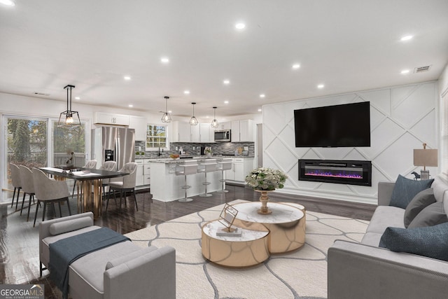 living room with a glass covered fireplace, recessed lighting, dark wood-style floors, and visible vents