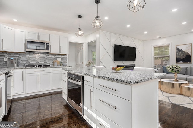 kitchen featuring dark wood-type flooring, backsplash, open floor plan, appliances with stainless steel finishes, and light stone countertops