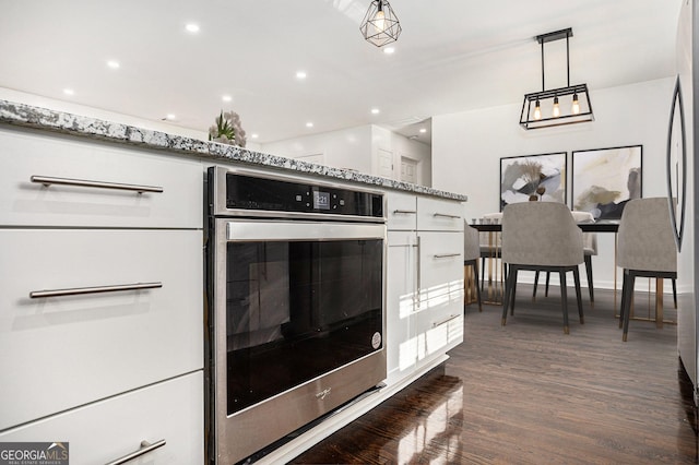 kitchen featuring oven, white cabinetry, light stone countertops, dark wood-style flooring, and hanging light fixtures