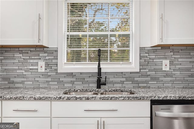 kitchen with stainless steel dishwasher, white cabinets, backsplash, and a sink