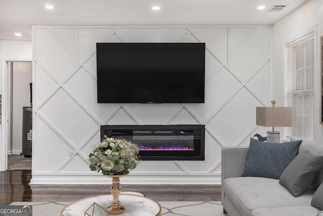 living area with visible vents, wood finished floors, a decorative wall, and a glass covered fireplace