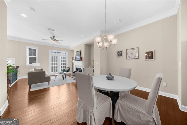 dining area featuring baseboards, a lit fireplace, wood finished floors, and crown molding