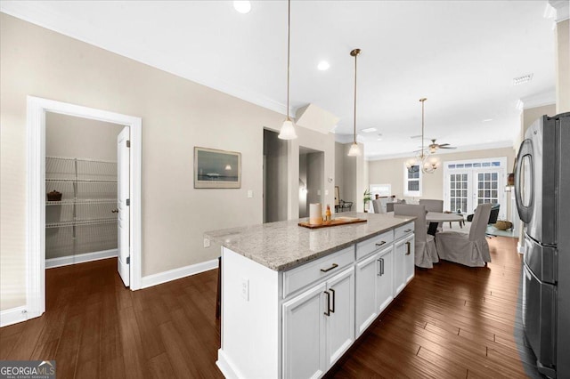 kitchen with a kitchen island, light stone countertops, freestanding refrigerator, white cabinetry, and dark wood-style flooring