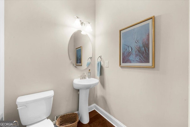 half bath featuring a sink, baseboards, toilet, and wood finished floors