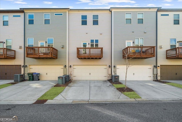 rear view of property with an attached garage, central AC unit, and driveway