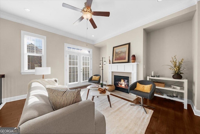 living area featuring a glass covered fireplace, wood finished floors, baseboards, and ornamental molding