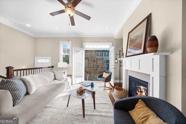 living area featuring wood finished floors, a glass covered fireplace, recessed lighting, crown molding, and ceiling fan