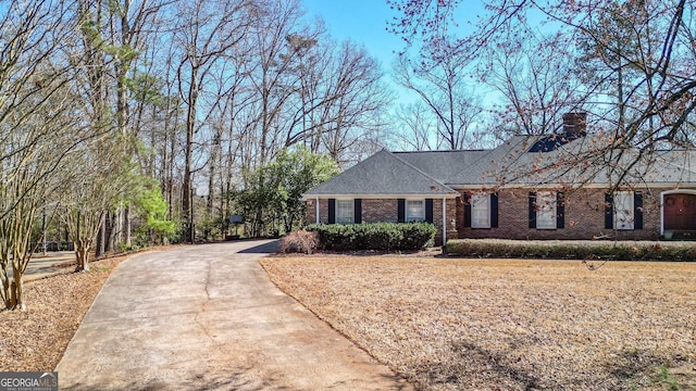 ranch-style house featuring driveway, a chimney, and brick siding