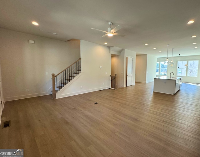 unfurnished living room featuring stairway, visible vents, wood finished floors, and recessed lighting