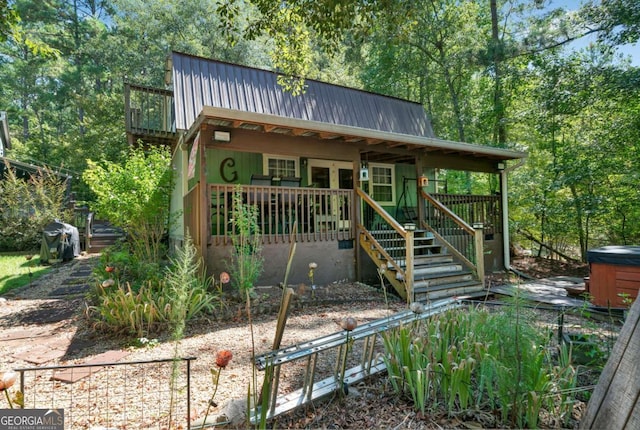 view of front of house featuring a hot tub, metal roof, a deck, a forest view, and stairs