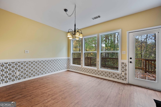 unfurnished dining area featuring a wainscoted wall, plenty of natural light, visible vents, and wood finished floors