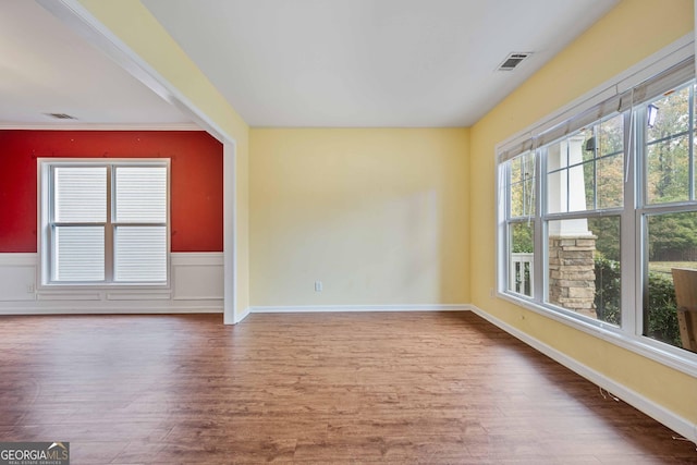 empty room featuring a wainscoted wall, wood finished floors, visible vents, and baseboards