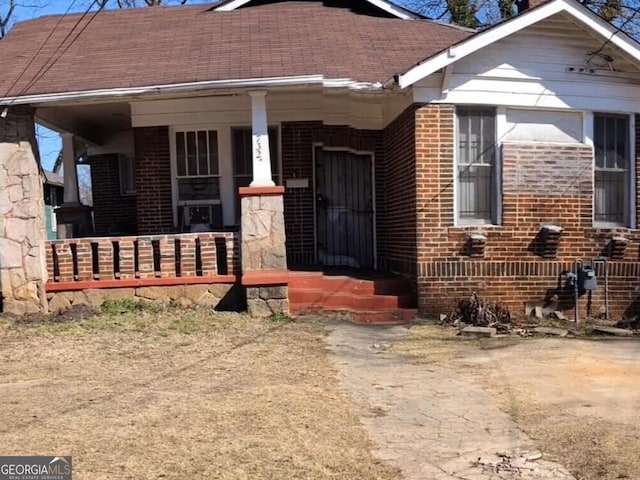 view of exterior entry featuring a porch, brick siding, and a shingled roof