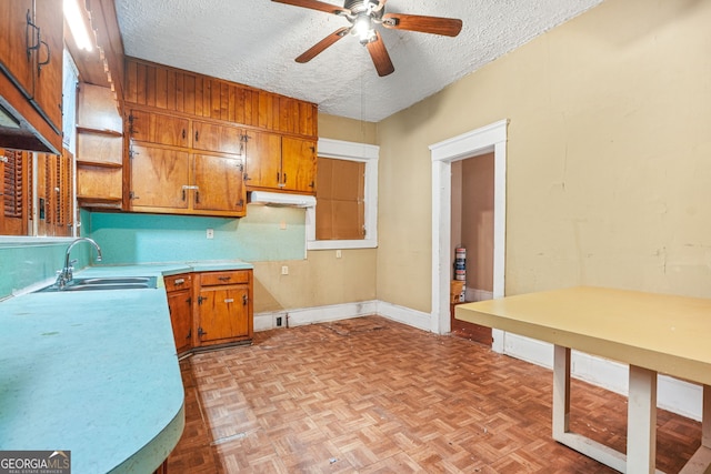 kitchen with brown cabinets, a ceiling fan, a sink, baseboards, and a textured ceiling