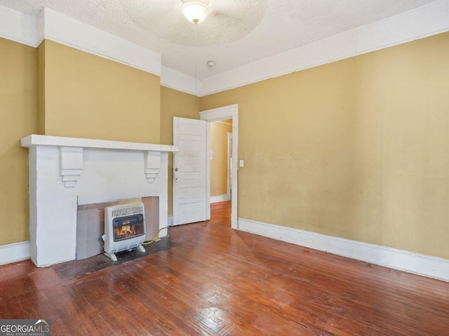 unfurnished living room with a textured ceiling, baseboards, heating unit, hardwood / wood-style floors, and a wood stove