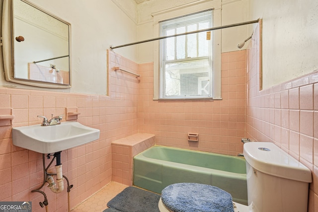 bathroom featuring shower / washtub combination, toilet, a sink, tile walls, and wainscoting