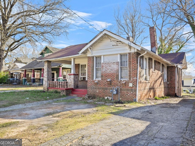 bungalow-style home featuring brick siding, a chimney, covered porch, and aphalt driveway