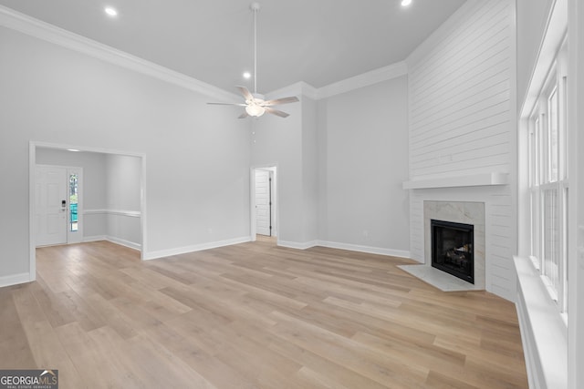 unfurnished living room featuring baseboards, ceiling fan, a premium fireplace, crown molding, and light wood-style floors