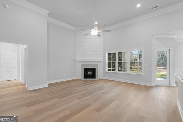 unfurnished living room featuring light wood finished floors, visible vents, a high ceiling, and ornamental molding