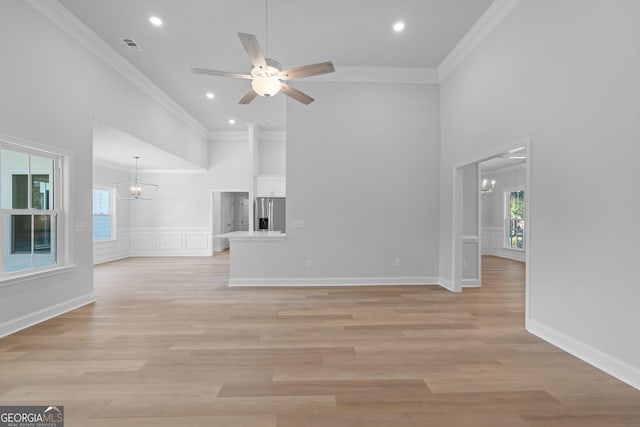 unfurnished living room with crown molding, a towering ceiling, light wood finished floors, and ceiling fan with notable chandelier