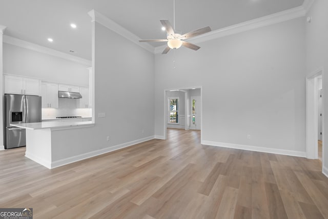 unfurnished living room featuring a towering ceiling, light wood-style floors, baseboards, and crown molding