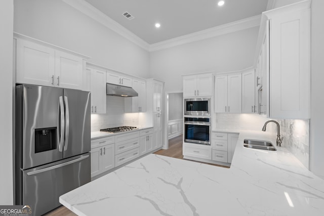 kitchen featuring appliances with stainless steel finishes, ornamental molding, white cabinets, a sink, and under cabinet range hood